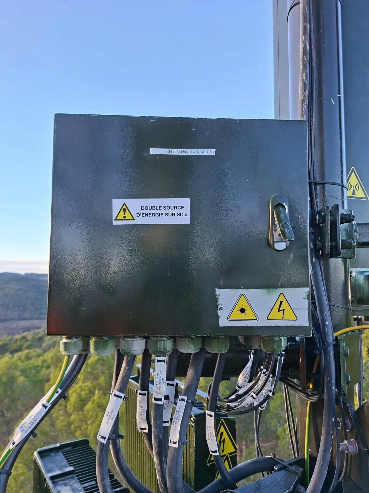 Coffret énergie camouflé vert avec étiquette « double source d'énergie sur site » et câbles repérés